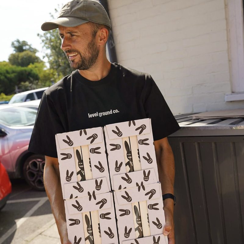 Team member in a Level Ground Co t-shirt carrying a stack of patterned coffee boxes