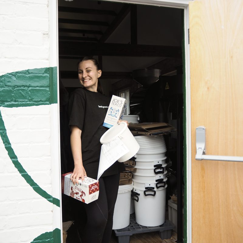 Team member in the roastery doorway holding tea boxes and a tub