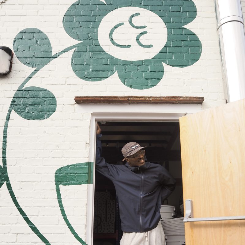 Team member in the roastery doorway beneath a painted flower mural